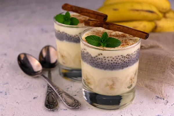 Two glasses with banana yogurt with cinnamon and chia seeds on a white plate. Close-up.