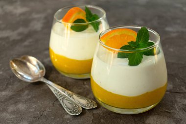 Portakallı kremalı maskot peyniri. İki bardak portakal aromalı tatlı ve gri arkaplanlı mascarpone.