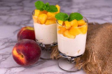 Two glasses of yogurt with peach on a white marble background.