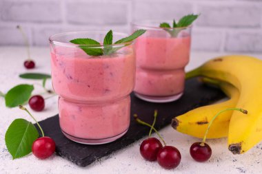 Pink cherry smoothies smoothies with fresh berries and banana on a black slate board.