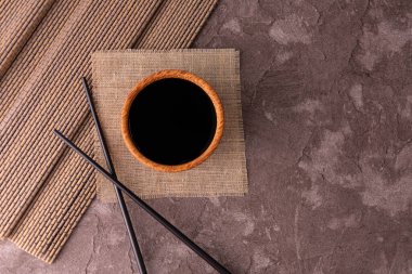 Ahşap bir kasede soya sosu ve gri arka planda yemek çubukları. Boşluğu kopyala.