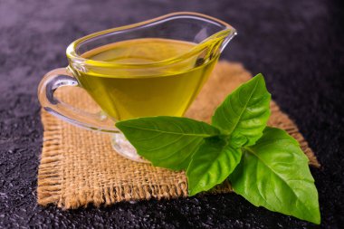 Cam tencerede zeytinyağı ve siyah arka planda fesleğen filizi. Yakın plan..