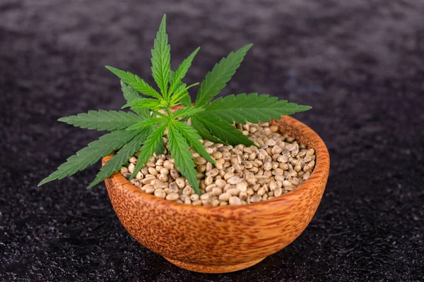 Healthy hemp seeds in a wooden bowl on a black background. Close-up.