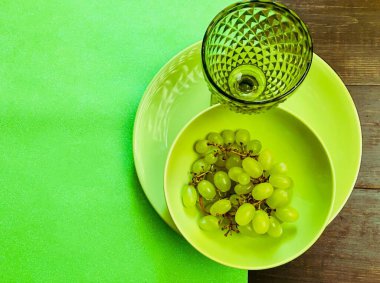 Üzümlü yeşil bir tabakta yeşil şarap kadehiyle servis edilen ağaçlık masa.