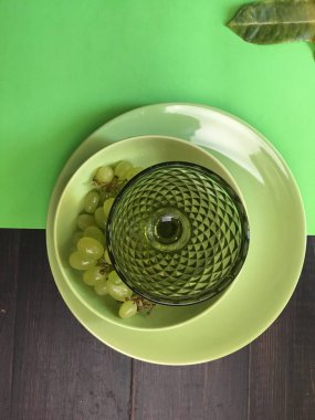 Üzümlü yeşil bir tabakta yeşil şarap kadehiyle servis edilen ağaçlık masa.