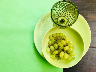 Üzümlü yeşil bir tabakta yeşil şarap kadehiyle servis edilen ağaçlık masa.