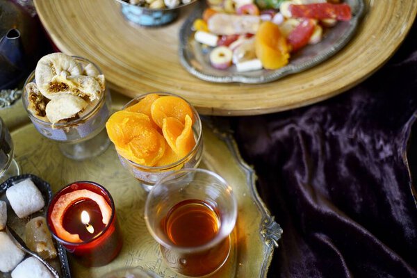 A table with Turkish tea with lale, oriental sweets, rahad delight, a mix of various nuts using copper dishes and bright fabrics.