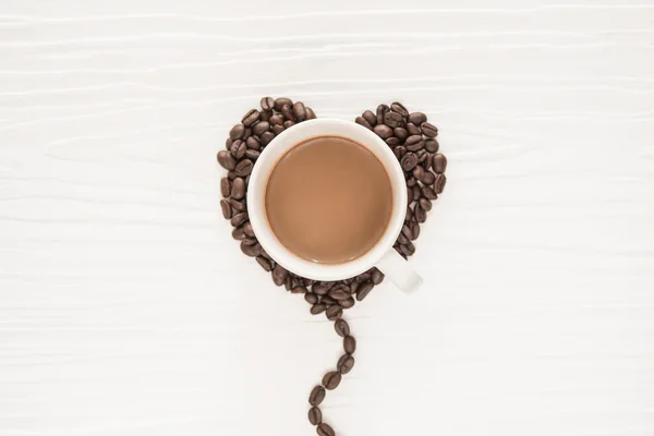 Кофейные зерна в форме сердец, чашка кофе на белом деревянном фоне — стоковое фото