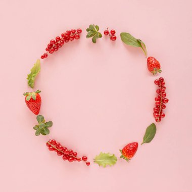 Çilek, frenk üzümü, mısır salatası, marul ve pastel pembe arka planda dairesel olarak düzenlenmiş ıspanak yapraklarından oluşan yaratıcı çerçeve. Kırmızı yaz meyveleri ve sebze sebzeleri düzdü. Minimum organik sağlıklı gıda düzenlemesi.