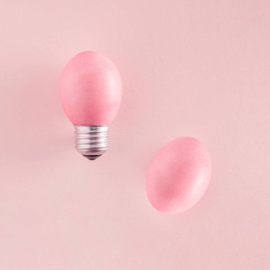 Hassas pembe Paskalya yumurtası ve pastel pembe arka planda izole edilmiş ampulden yapılmış yaratıcı bir fikir. Estetik Paskalya Festivali dokusu fikri. Minimum düzlük.