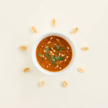 Fıstık çekirdekleri, fındık ezmesi soslu ve pastel bej arka planda Afrika baharatlı fındık ezmesi soslu kâsenin etrafında daire şeklinde dizilmiş. Minimum organik, doğal, sağlıklı besinler yaz konsepti.