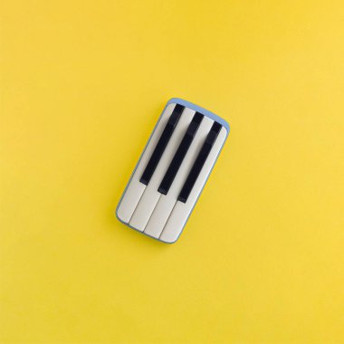 Piyano tuşlu gri cep telefonundan yapılmış yaratıcı bir düzen. Sarı arka planda izole edilmiş. Müzik iletişimi eğlenceli bir fikir. Minimum estetik, soyut, düz konsept, sürreal konsept.
