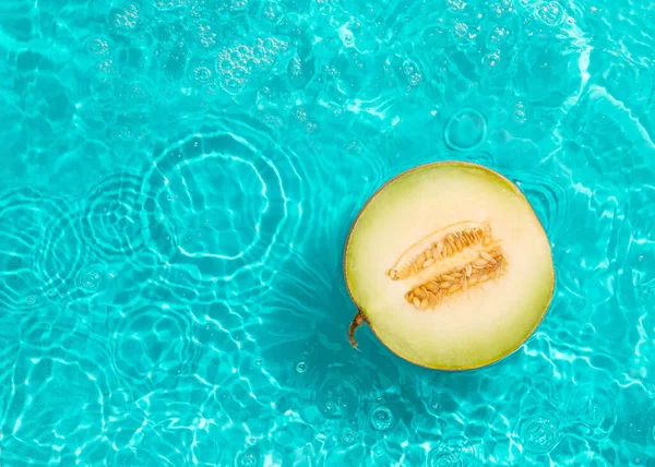 Halved cantaloupe melon in the bright blue turquoise water with reflections of the sun and shadows. Natural creative summer fruit background. Beach or swimming pool vacation. Refreshing, leisure, party concept. Minimal flat lay.