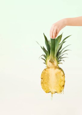 Childs 'ın el ele tutuşması, olgunlaşmış, sulu ananas ve soluk yeşil bej arka planda izole edilmiş meyve suyu damlaları. Doğal tropik yaz meyvesi. Organik, çiğ, sağlıklı, yiyecek, minimum konsept.
