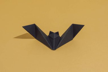 Origami yarasası siyah kağıttan yapılmış, altın ya da ocher arkaplanda izole edilmiş. Fotokopi odasıyla dekorasyon konseptini kendin yap. Güneş ve gölgeler. Cadılar Bayramı partisi için en az lüks davetiye kartı.