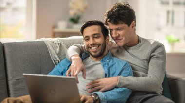 Tatlı eşcinsel çift evde vakit geçirir. Bir kanepeye uzanıp dizüstü bilgisayarı kullanıyorlar. İnternete göz atıyorlar. Partners Hand onun sevgilisinin yanında. Gülümsüyorlar ve gülüyorlar. Odanın Modern İçi Var.