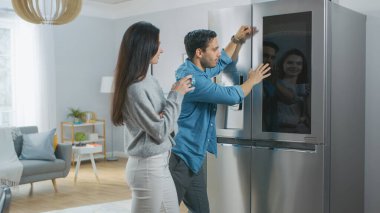 Güzel genç çift sabah kahvesini mutfakta içiyor. Evdeki Akıllı Buzdolabında hava durumunu ve yapılacaklar listesini kontrol ediyorlar. Daire Parlak ve Konforlu.