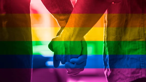 Close-Up of Two Male Hands Gently Touching and Hold Each Other. Cute Queer Relationship Concept. Gay Couple are Casually Dressed. Room is Bright and Sunny. Shot has Freedom Rainbow Flag Filter on it — Stock Photo, Image