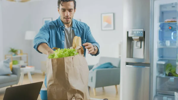 Schöner junger Mann bringt Lebensmittel in die Küche Er kaufte frisches Salatgemüse. Moderne Kühlschränke sind im Hintergrund. Zimmer hat helles modernes Interieur. — Stockfoto