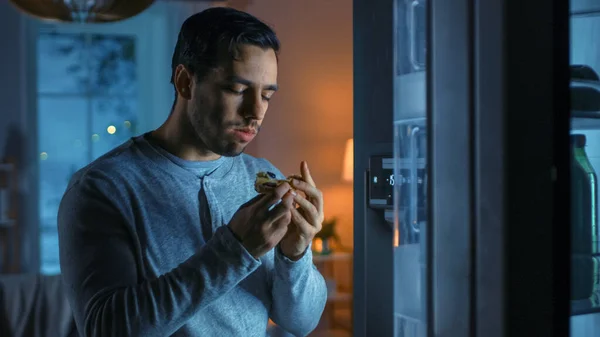 Por la noche en la cocina guapo joven atractivo está comiendo una pizza sobrante de la nevera. Está hambriento y se siente satisfecho. —  Fotos de Stock