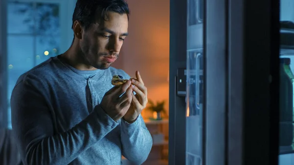 V noci v kuchyni pohledný atraktivní mladý muž jí zbytky pizzy z ledničky. Je hladový a cítí se spokojený. — Stock fotografie