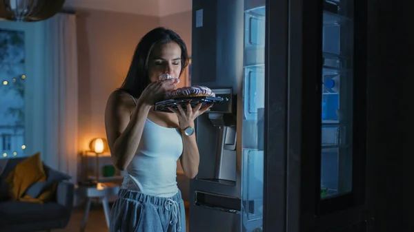 Hungry Beautiful Young Woman in the Kitchen in the Evening Opened the Fridge, Takes out a Piece of a Delicious Creamy Cake and Starting to East it. She Feels Satisfied. — Stock Photo, Image