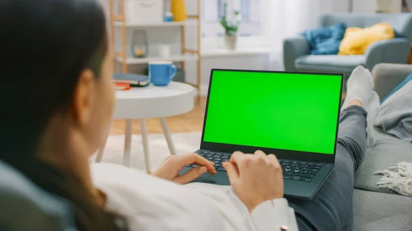 自宅の女性緑のモックアップ画面とラップトップコンピュータ上で作業ソファに横たわっています.インターネットやソーシャルネットワークの閲覧のためのコンピュータを使用して女の子.肩のショットの上に. — ストック写真