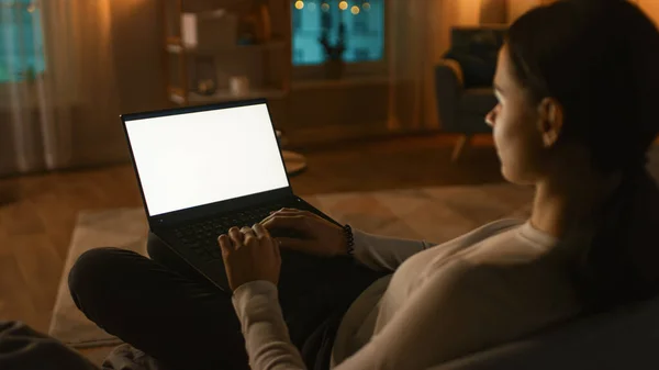 自宅での夜:若い女性は、ホワイトモックアップスクリーンラップトップコンピュータで使用してソファに休んでいます。Girl Using Chroma Key Notebook for Internet Browsing, Post on Social Networks. — ストック写真