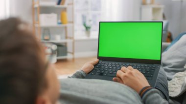 Green Mock Ekran Bilgisayarı ile Kanepede Uzanmış Adam. Guy Laptop Cihazı Kullanıyor, İnternet Taranıyor, İçerik İzleniyor, Videolar.