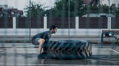 Spor Giysileri ve Eldivenleri Giyen Güçlü Kaslı Genç Adam Açık Hava Basketbol Sahasında Egzersiz Yapıyor. Bir İkindi Yağmurdan Sonra Bir Konutta Büyük Bir Tekerleği Döndürüyor