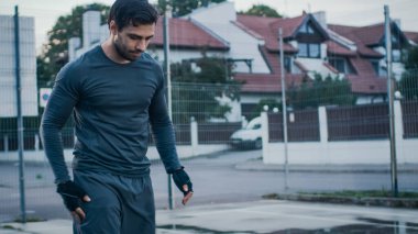 Spor Giysileri ve Eldivenleri Giyen Güçlü Kaslı Genç Adam Açık Hava Basketbol Sahasında Egzersiz Yapıyor. Yürüyor ve aşağı bakıyor. İkindi Yağmurdan Sonra Mahallede
