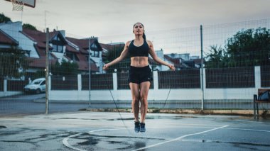 Beautiful Energetic Fitness Girl Skipping Jumping Rope. She is Doing a Workout in a Fenced Outdoor Basketball Court. Afternoon After Rain. clipart
