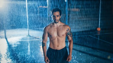 Güçlü, kaslı, formasız genç adam spor egzersizlerini tamamlıyor. Gece Şiddetli Yağmurda Arkasında Bir Işık ile Tezahürat Yapıyor.