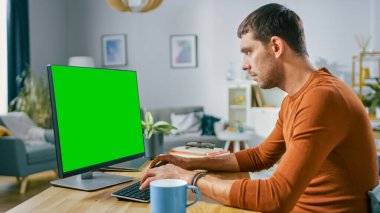 Evde Masasında oturan Yakışıklı Gülümseyen Adam Mock-up Green Screen ile Kişisel Bilgisayarı Kullanıyor. Modern Oturma Odası 'nın iç mekânında çalışıyor..