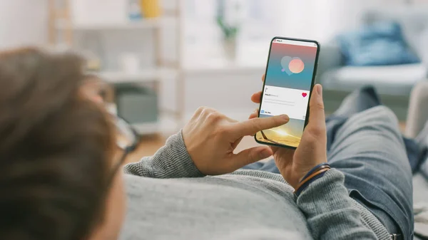 Homme à la maison Allongé sur un canapé à l'aide d'un téléphone intelligent, Faire défiler les médias sociaux, Vérifier les nouvelles, Activité des amis. Guy utilisant le téléphone mobile, Internet Réseaux sociaux Navigation sur. — Photo