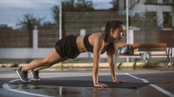 Beautiful Energetic Fitness Girl Doing Push Up Exercises. She is Doing a Workout in a Fenced Outdoor Basketball Court. Evening After Rain in a Residential Neighborhood Area. — Stock Photo, Image