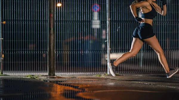 Menina Aptidão Energética bonita é Sprinting em uma quadra de basquete ao ar livre cercada. Ela corre à noite depois da chuva em uma área residencial de vizinhança. — Fotografia de Stock