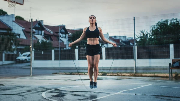 Menina Aptidão Energética bonita pulando corda de salto. Ela está fazendo um treino em uma quadra de basquete ao ar livre cercada. Tarde após a chuva. — Fotografia de Stock