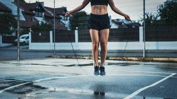 Menina Aptidão Energética bonita pulando corda de salto. Ela está fazendo um treino em uma quadra de basquete ao ar livre cercada. Tarde após a chuva em uma área residencial de vizinhança. — Fotografia de Stock
