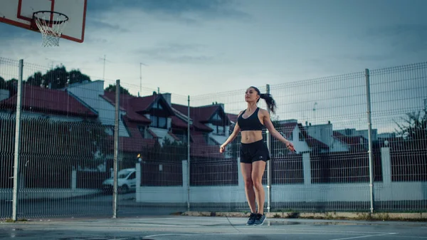 Gyönyörű Energetikus Fitness Lány Ugráló Ugráló Kötél. Edzést tart egy bekerített szabadtéri kosárlabdapályán. Esti lövés esőzés után a lakóövezetben. — Stock Fotó