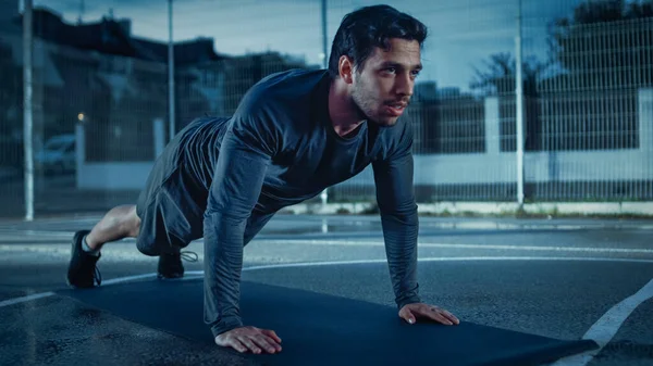 Sterke gespierde jonge man in sportkleding die oefeningen doet. Hij doet een workout in een omheind Outdoor Basketbalveld. 's Avonds neergeschoten na regen in een woonwijk. — Stockfoto