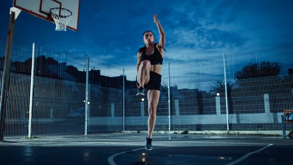 Hermosa Energetic Fitness Girl Hacer ejercicios. Ella está haciendo un entrenamiento en una cancha de baloncesto al aire libre vallada. Disparo nocturno después de la lluvia en un barrio residencial. —  Fotos de Stock