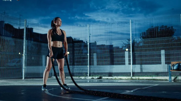Beautiful Energetic Fitness Girl Doing Exercises with Battle Ropes (англійською). Завершив професійну ігрову кар'єру в баскетбольному суді. Вечір після дощу в сусідньому районі. — стокове фото