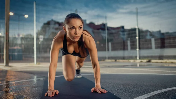 Hermoso Energetic Fitness Girl Hacer ejercicios de escalador de montaña. Ella está haciendo un entrenamiento en una cancha de baloncesto al aire libre vallada. Noche después de la lluvia en un barrio residencial. —  Fotos de Stock