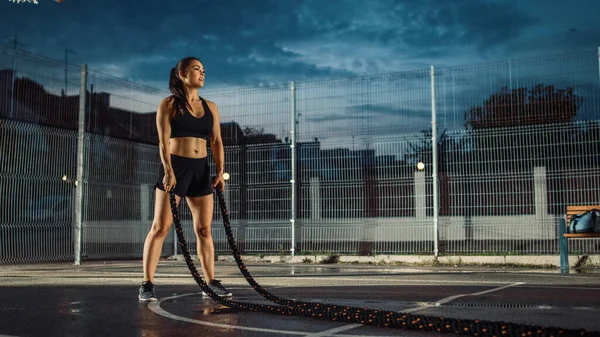 Vackra Energetic Fitness Girl gör övningar med Battle Ropes. Hon gör ett träningspass i en inhägnad utomhus basket domstol. Kvällstid efter regn i ett bostadsområde. — Stockfoto