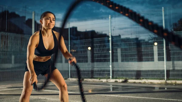 Beautiful Energetic Fitness Girl Doing Exercises with Battle Ropes (англійською). Виступає на професійному рівні в баскетбольному суді. Вечір після дощу в сусідньому районі. — стокове фото