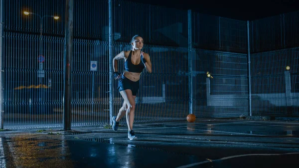 Menina Aptidão Energética bonita é Sprinting em uma quadra de basquete ao ar livre cercada. Ela corre à noite depois da chuva em uma área residencial de vizinhança. — Fotografia de Stock