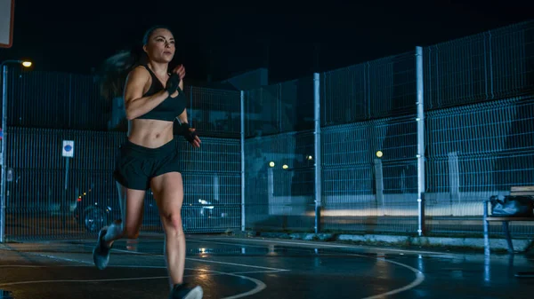 Schöne Energetic Fitness Girl sprintet in einem eingezäunten Outdoor-Basketballfeld. Geschäfte laufen nachts nach Regen in Wohngebiet. — Stockfoto