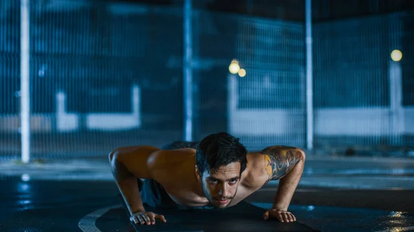 Forte Muscular Fit Shirtless Young Man está fazendo exercícios push-up. Ele está fazendo um treino em um campo de basquete ao ar livre cercado. Noite após a chuva em uma área de vizinhança residencial. — Fotografia de Stock