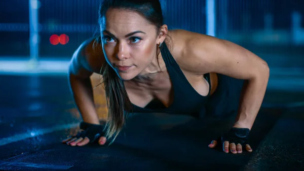 Gyönyörű Sportos Fitness Girl csinál push up gyakorlatok. Edzést tart egy bekerített szabadtéri kosárlabdapályán. Éjszakai felvételek esőzés után egy lakóövezetben. — Stock Fotó